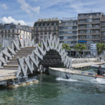 Photo montrant une barque à moteur passer sous la passerelle relevée en arc.